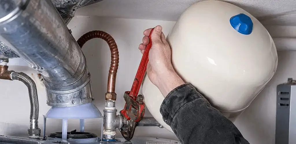 Water heater repair technician tightening plumbing connections near a tank unit in Baltimore, MD